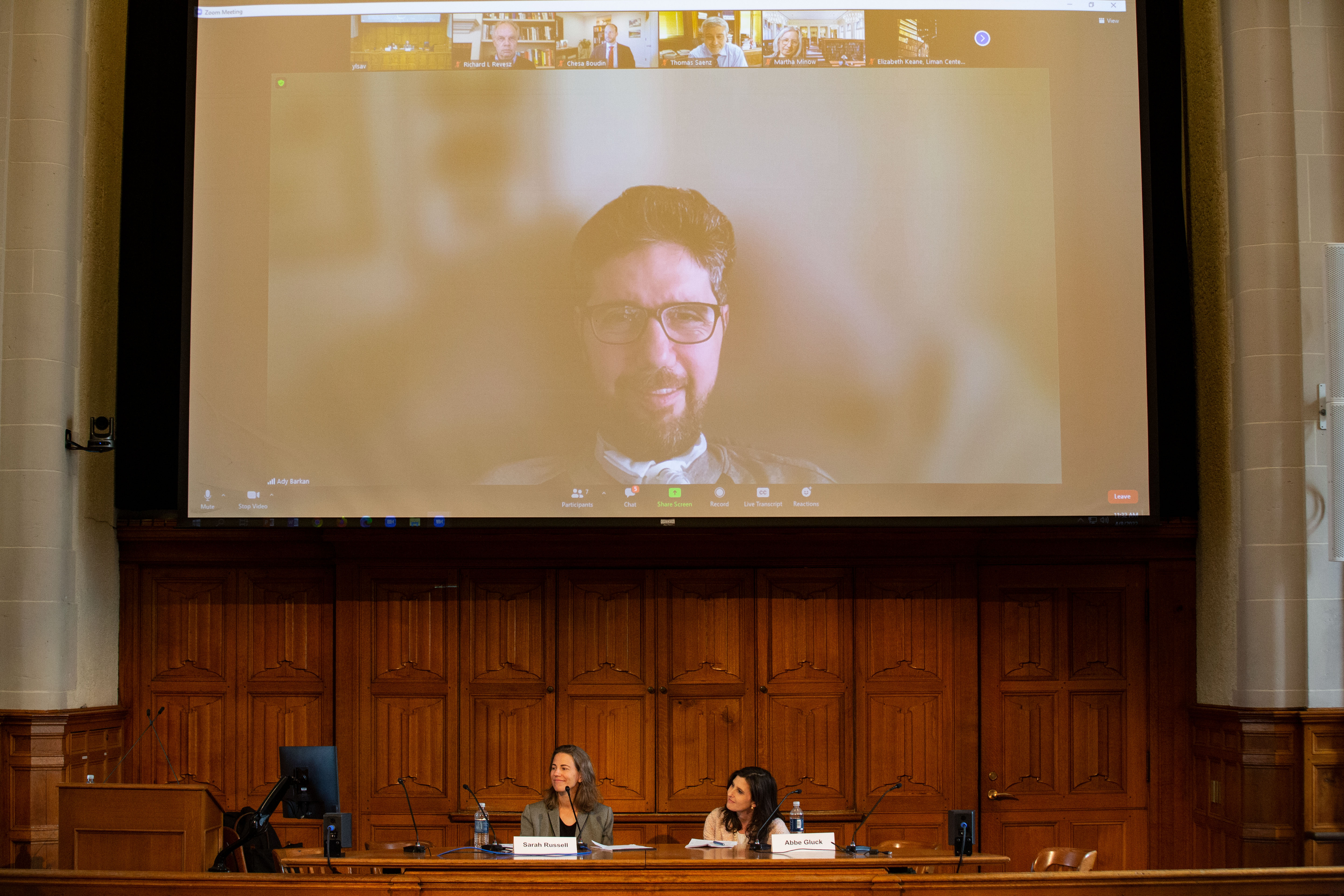Ady Barkan’s face is shown on a large projection screen above the panelists’ table in an auditorium