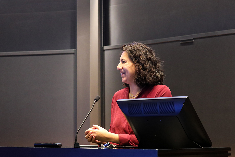 Professor Anika Singh Lemar, in profile, standing in a classroom behind a microphone and podium