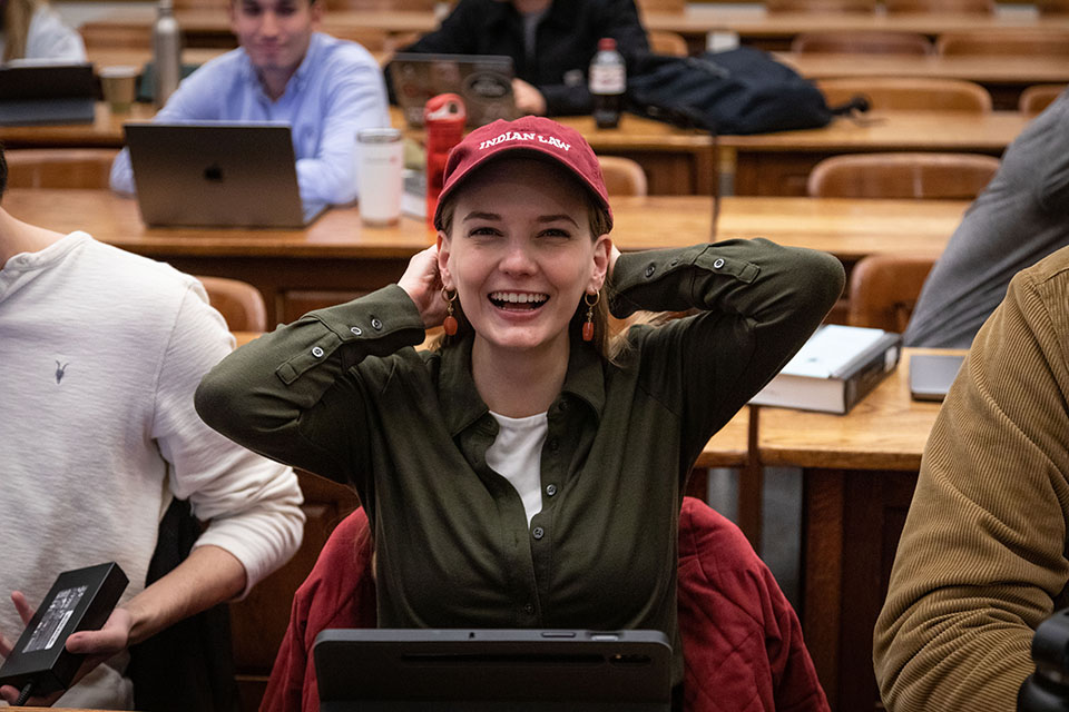 A student wearing a baseball cap with the words "Indian Law" stretches in class.