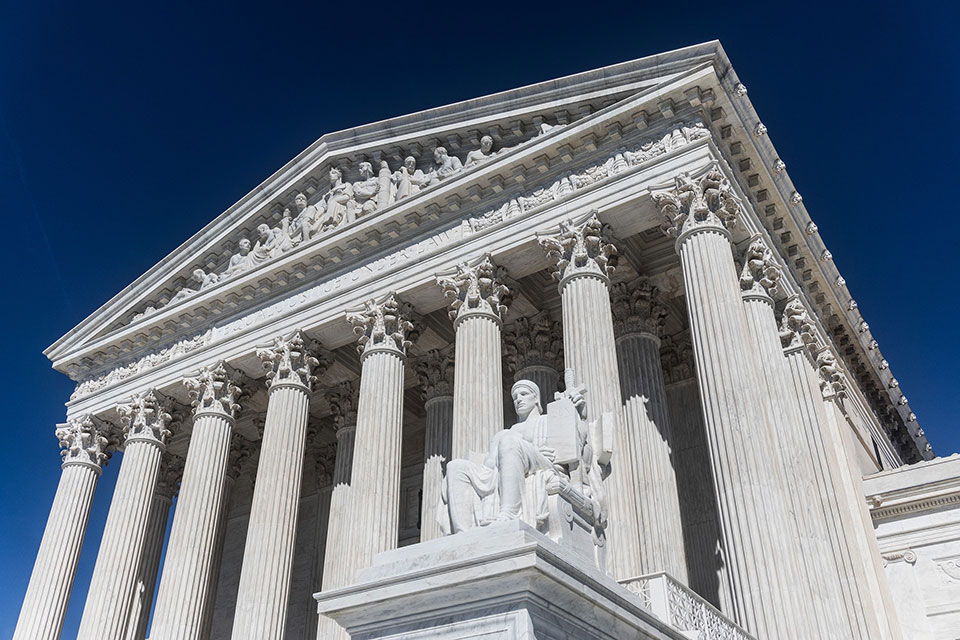 The Supreme Court of the United States building and its Authority of Law statue surrounded by blue sky