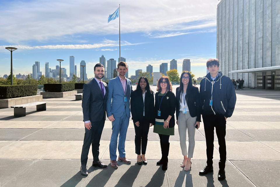 A group of students standing in a concrete plaza with the U.N. flag and the New York skyline behind them