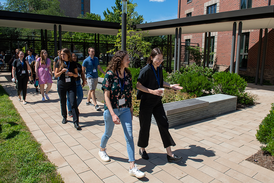 A group of students walking into the Baker Hall courtyard through a gate and across a walkway