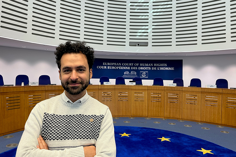 Yussef Al Tamimi stands in a large room with a long judges' bench and row of chairs. A sign on the wall above the seats reads "European Court of Human Rights" in English and French