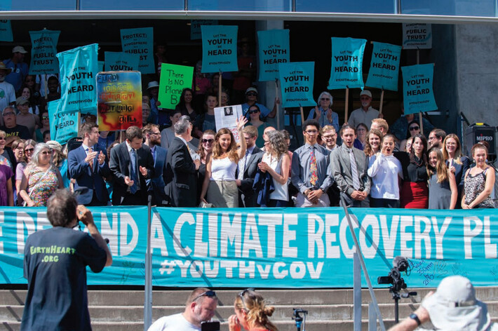 A group of people stand at a climate march in front of a banner reading We Demand a Climate Recovery Plan