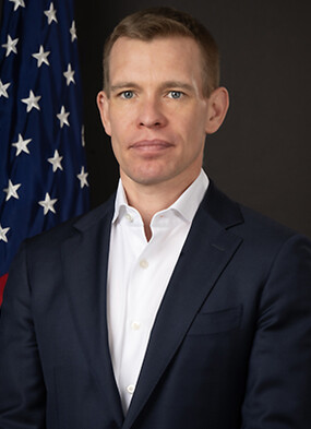 A headshot of Matthew R. Christiansen standing in front of an American flag.