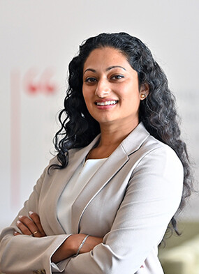 Anjali Pathmanathan stands smiling at the camera with her arms crossed.