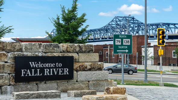 a sign says "Welcome to Fall River" in front of a large bridge