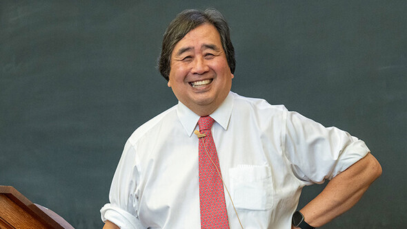 Harold Koh stands smiling in front of a blackboard with his shirtsleeves rolled up