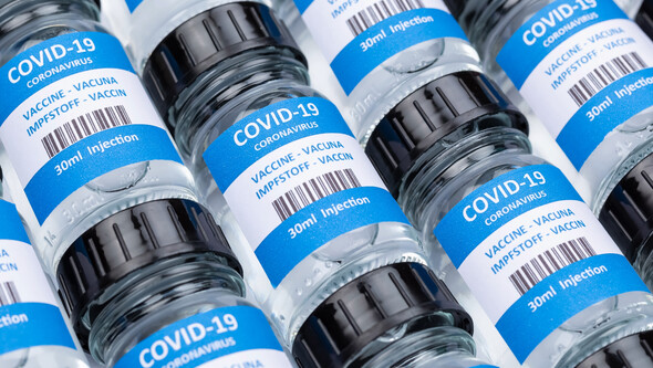 rows of glass vials with a label showing the words "COVID-19" and "VACCINE."