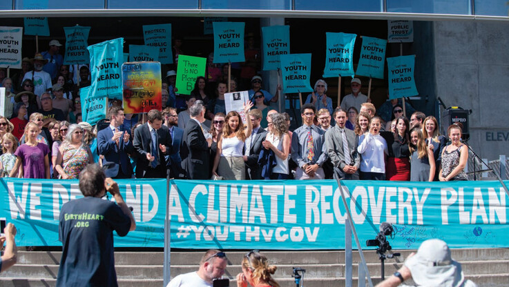 A group of people stand at a climate march in front of a banner reading We Demand a Climate Recovery Plan