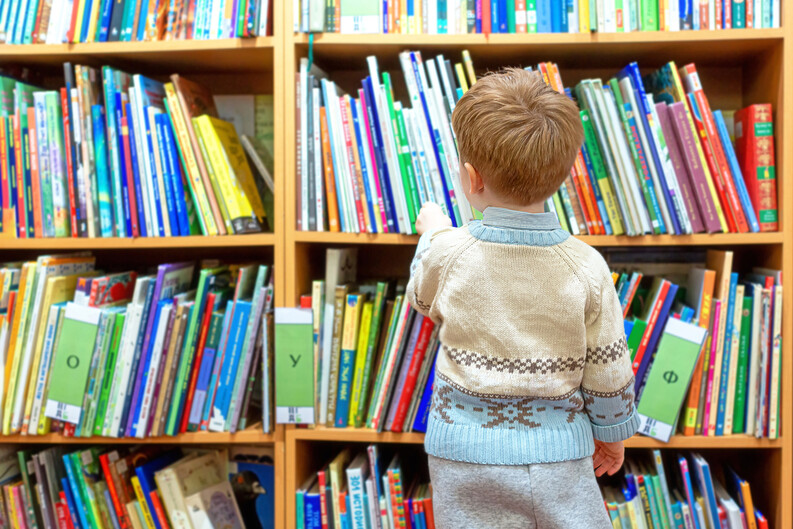 Child in a sweater browsing a shelf of books