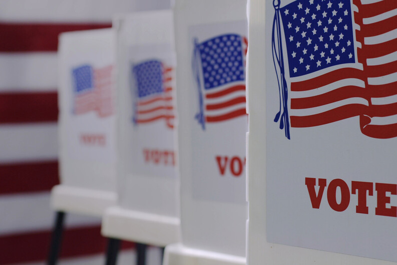 A row voting booths, each emblazoned with an American flag and the word "VOTE."