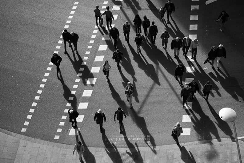 A black and white image of pedestrians crossing a street in a crosswalk shown from above