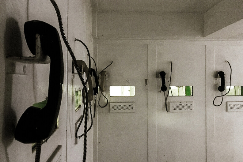 A row of wall-mounted telephones in a dimly-lit room with grimy walls