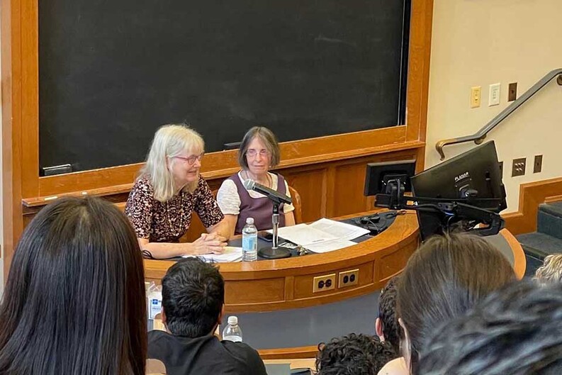 Victoria A. Cundiff ’80, left, is seated in front of a chalkboard with Roberta Romano ’80 in front of an audience of students
