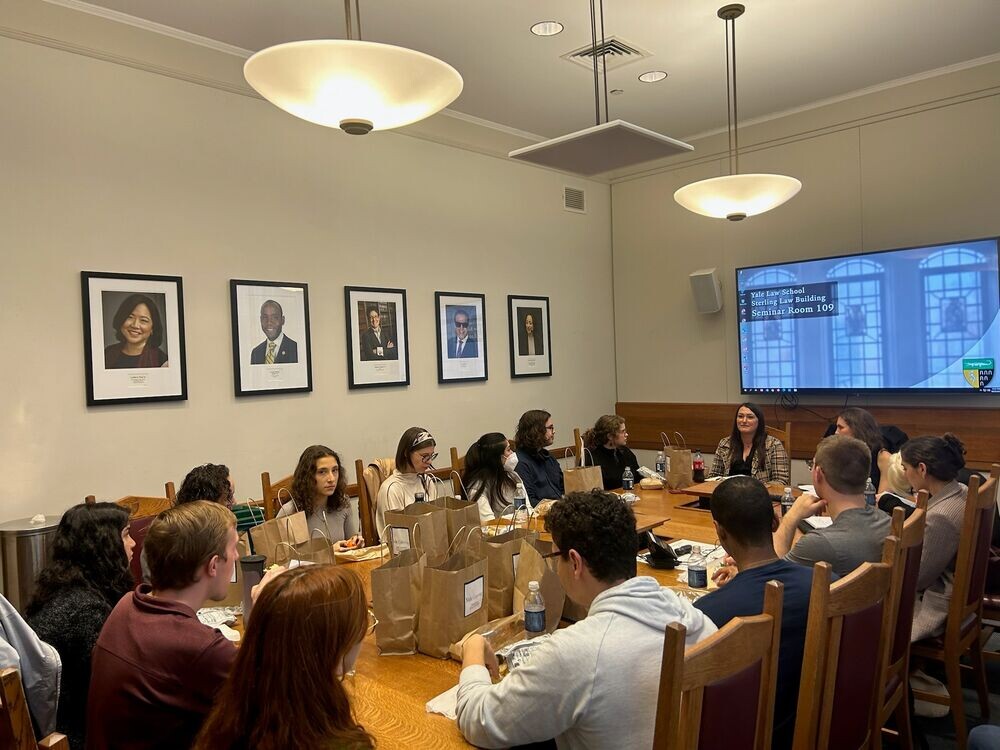 Students seated around a table in a seminar room at the law school listening to a female speaker