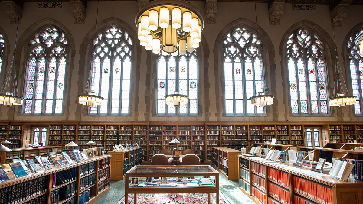 A wide view of the law library showing stained glass windows, elaborate lighting fixture, bookshelves, and a display case on top of an Oriental rug.