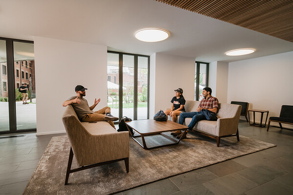 Students chatting in a seating area in Baker Hall with contemporary windows, gray floor, and modern furniture.