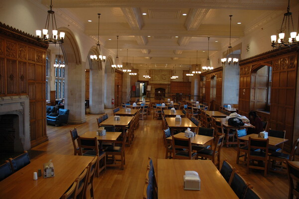 The Ruttenberg Dining Hall wood paneling and a fireplace along with dining tables and chairs.