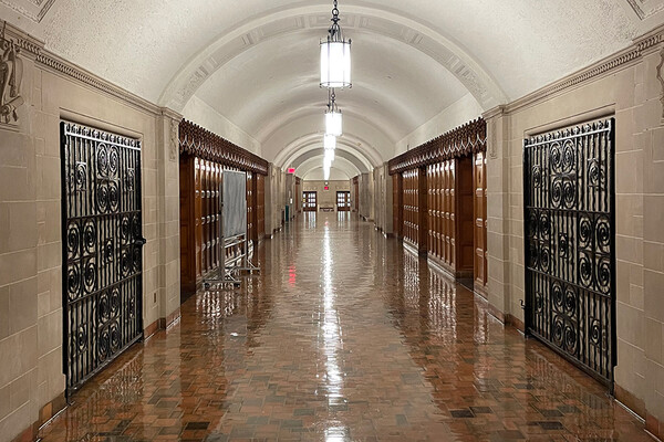the long well-lit main hallway with arched white ceiling, walls of stone, ornate wood paneling, and a polished tile floor