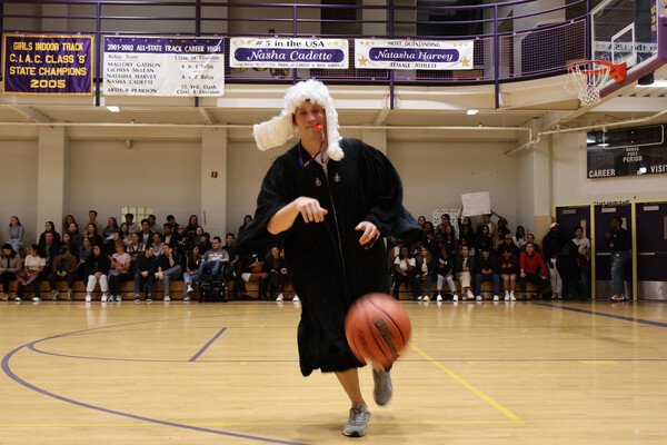 A student wearing a judge's robe and wig runs on the basketball court
