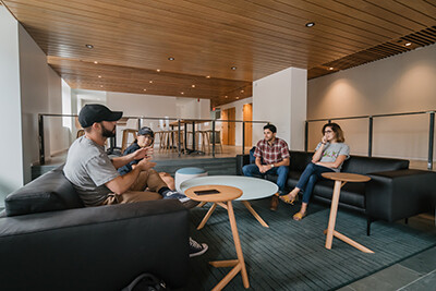 Four students sit in a circle around a coffee table in a Baker Hall student lounge.