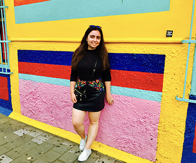 A young woman standing in front of a brightly painted exterior wall