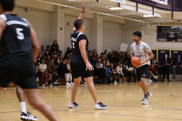 A basketball player about to pass the ball. Another player defends with his arm up.