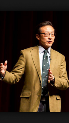 Joe Tsai speaking and gesturing with his hands in front of a dark background