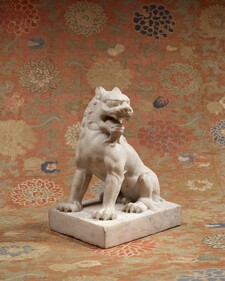 A sculpture of a lion in white stone with its head turned to the side and mouth open