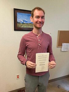 Andy Udelsman stands holding a document