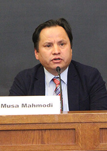 Musa Mahmodi speaks into a microphone with a name card in front of him on a table