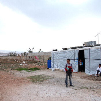 Three Syrian children standing next to a UNICEF-branded, white tarp tent.