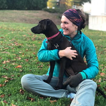 Hannah Duncan seated on grass with a black lab dog