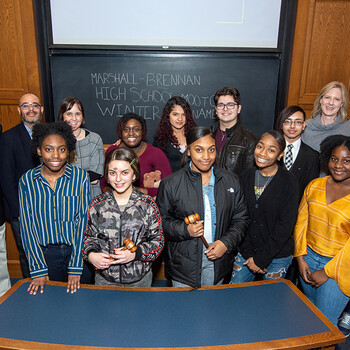 A group of students and teachers pose in front of a blackboard reading Marshall-Brennan High School Moot Court