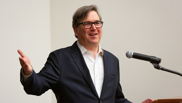 Jason Furman speaks at a microphone with his right arm raised