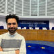 Yussef Al Tamimi stands in a large room with a long judges' bench and row of chairs. A sign on the wall above the seats reads "European Court of Human Rights" in English and French