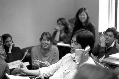 Harold Koh talks on the phone with students smiling in the background