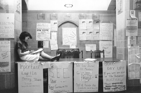 A female student sits in profile on the table surrounded by posters for student events