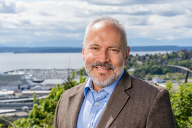 Jorge Barón ’03 standing outside with green hills and a body of water in the background.