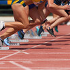 Female runners legs as they leave the starting blocks of a race, running on a reddish track with white stripes 