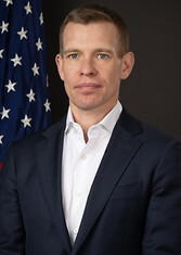 A headshot of Matthew R. Christiansen standing in front of an American flag.