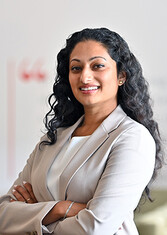 Anjali Pathmanathan stands smiling at the camera with her arms crossed.