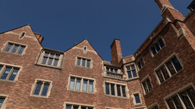 An interior-facing brick façade of Sterling Law Building with multiple pitched rooflines and stone-trimmed, leaded glass windows against a dark blue sky