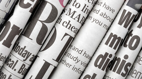 A stack of folded newspapers with a few letters of headlines visible on each