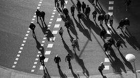 A black and white image of pedestrians crossing a street in a crosswalk shown from above
