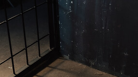 Prison bars cast shadows the floor in a dark prison cell