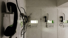 A row of wall-mounted telephones in a dimly-lit room with grimy walls