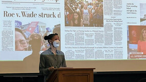 Khiara Bridges at podium before a projection screen with headlines about Dobbs v. Jackson Women’s Health Organization and other abortion-related court cases.