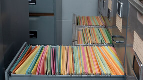 A filing cabinet with an open drawer, revealing colorful hanging file folders